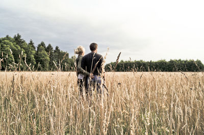 Rear view of man and woman standing on grassy field against sky