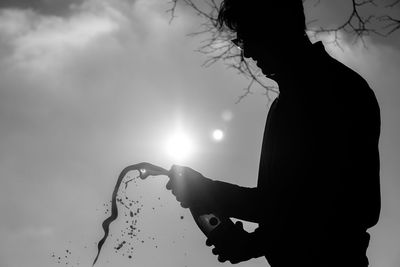 Silhouette man popping champagne while standing against sky