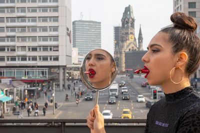 Woman carrying toy car in mouth by mirror in city