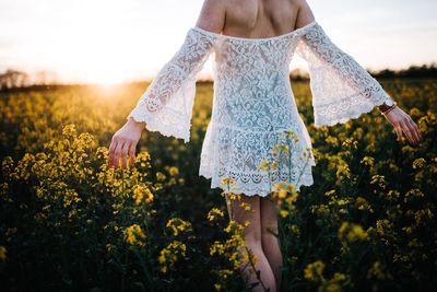 Midsection of woman standing amidst flowers against sky during sunset