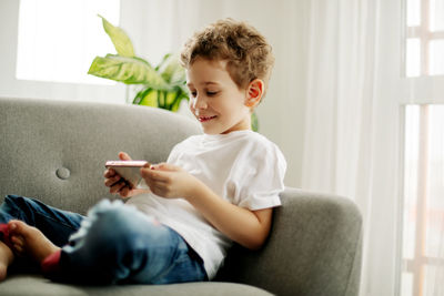 A cheerful boy with a phone in his hands is sitting in a chair and playing a game 