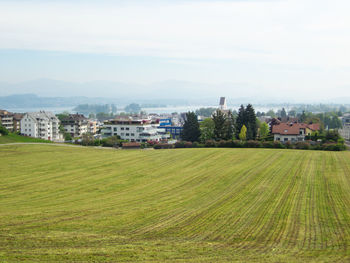 Scenic view of field by houses against sky