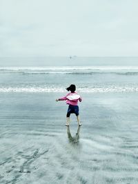 Rear view of excited girl at sea shore against sky