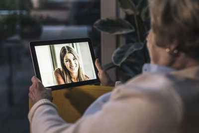 Senior woman on video call with granddaughter through digital tablet at home