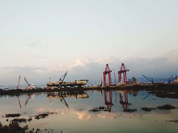 Cranes at commercial dock against sky during sunset