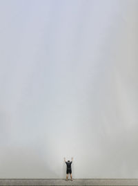 Tiny man standing facing a huge blank white wall