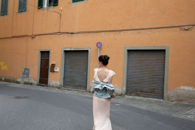 Rear view of woman standing on footpath against building