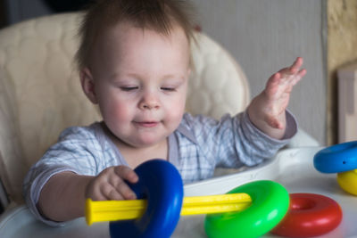 Cute baby boy playing with multi colored plastic toy on high chair at home