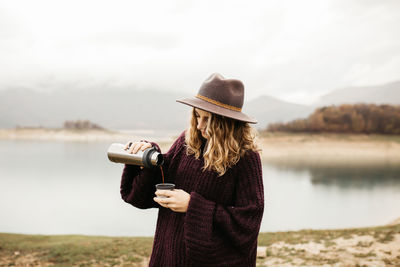 Man wearing hat standing by lake against sky