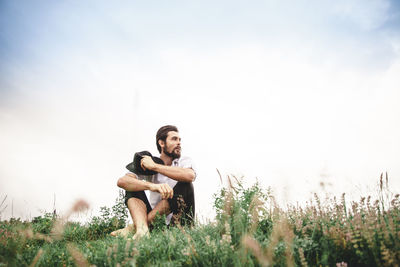 Full length of thoughtful young man looking away while sitting on grassy field