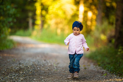 Full length of baby girl walking on dirt road amidst forest