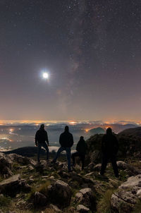 Silhouette people standing on cliff against sky at night