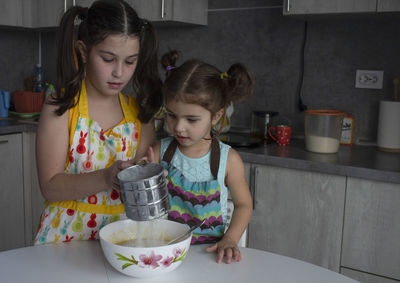 Lovely sisters pour the flour together at home