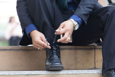 Low section of businessman tying shoelace while sitting on the wall