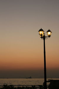 Street light by sea against sky during sunset