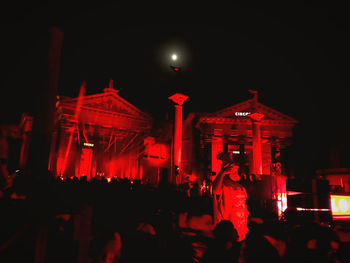 People in illuminated city against sky at night