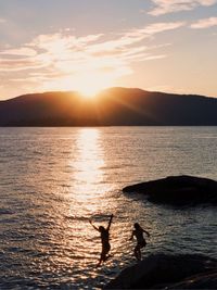 Silhouette people on sea against sky during sunset