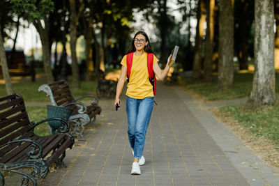 A happy young girl with a book in her hands walks through the park after lectures at the university