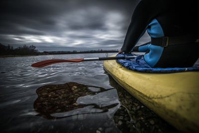 Midsection of man sitting in kayak on lake against stormy clouds