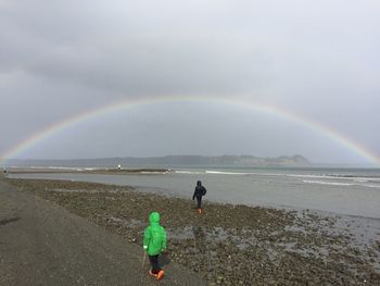 Rear view of people walking on beach against rainbow