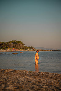 Man standing at beach against sky during sunset