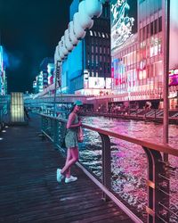 Rear view of woman walking by illuminated buildings in city at night