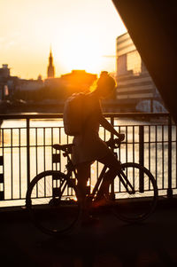 Silhouette man riding bicycle on bridge against sky during sunset