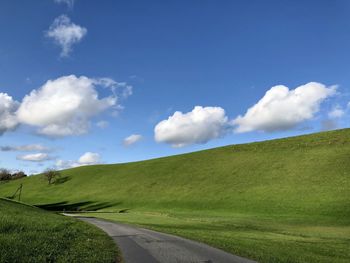 Empty road amidst field against sky