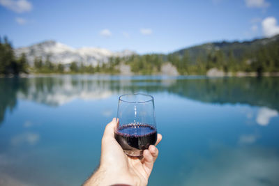 Man holds glass or red wine at the lake.