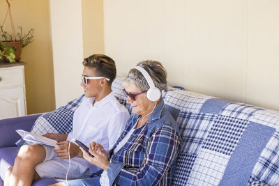 Senior woman with grandson listening to music while sitting on sofa at home