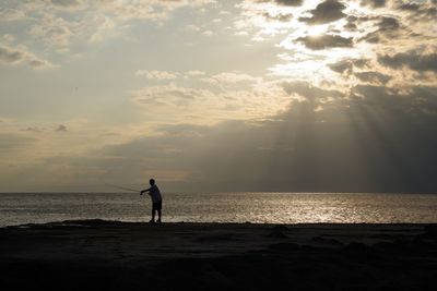 Silhouette man standing on beach against sky during sunset