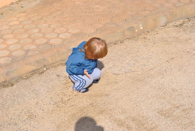 High angle view of boy crouching on footpath