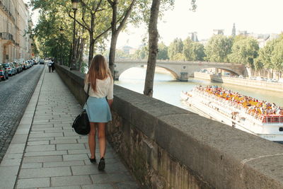 Rear view of woman walking on footpath by seine river