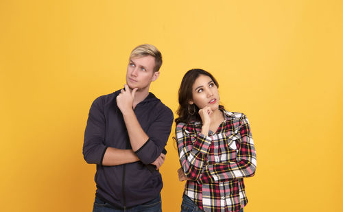 Portrait of young couple standing against yellow background