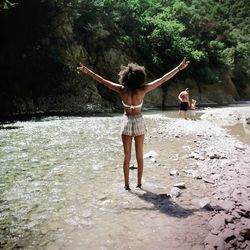 Rear view of woman with arms raised standing in water