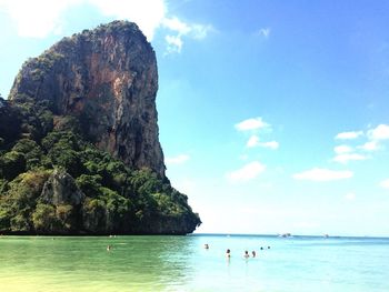 People in sea by rock formation against sky