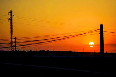 Silhouette electricity pylon on field against orange sky