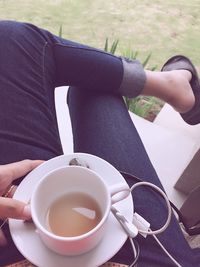 Low section of woman having coffee while sitting outdoors