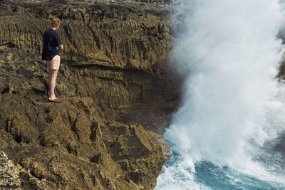 Rear view of woman standing on cliff by sea