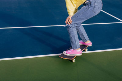 Low section of woman standing on skateboard on a tennis court 
