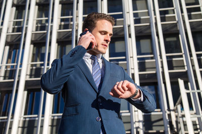 Low angle view of businessman talking on smart phone while standing against building