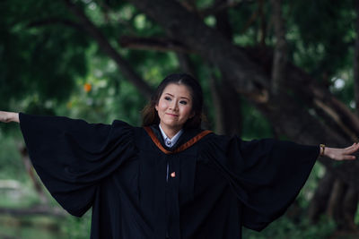 Portrait of young woman standing against trees