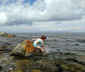 Rear view of man on rock at beach against sky