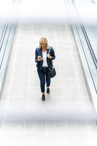 Smiling businesswoman using phone walking on walkway