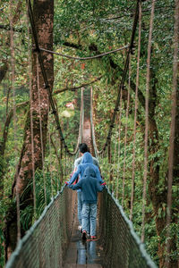 Rear view of family walking on footbridge in forest