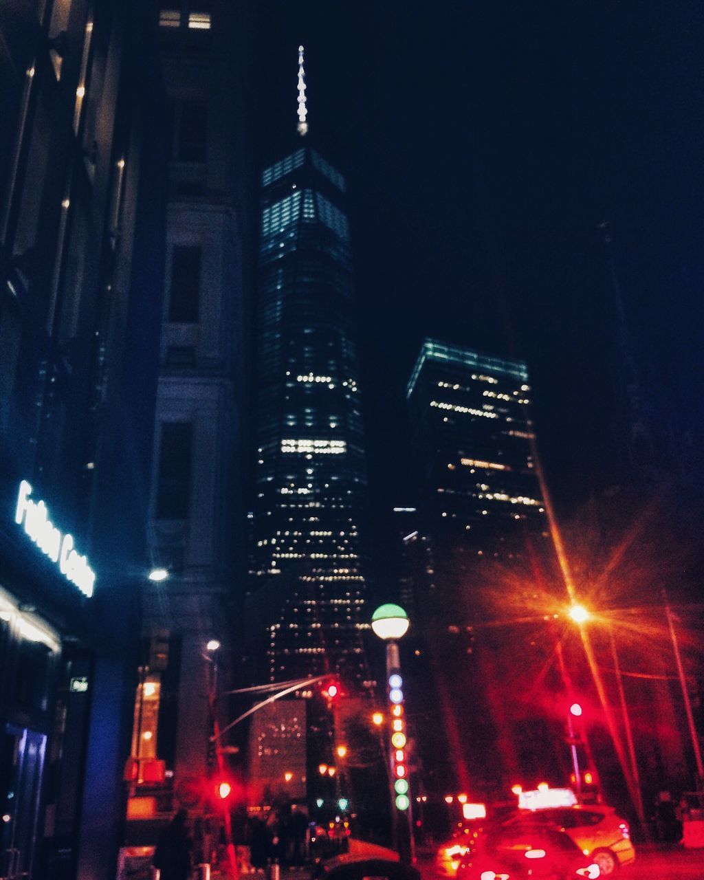 illuminated, building exterior, architecture, night, built structure, city, tall - high, tower, transportation, street, skyscraper, city street, dark, city life, sky, tall, diminishing perspective, urban skyline, office building, tail light, outdoors, spire, modern, urban scene, the way forward