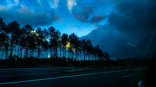 Silhouette trees by road against sky at night