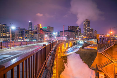 Illuminated street amidst buildings against sky at night