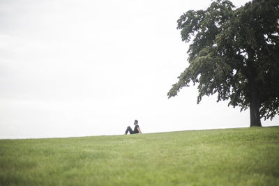 Mid distance view of man sitting on grassy field against sky
