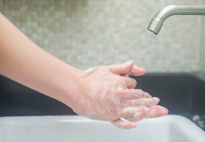 Cropped image of hand touching water from faucet in bathroom